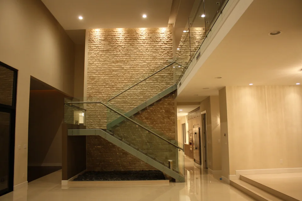 Sculptural staircase, glass railing, and stone feature wall in a Lemar home